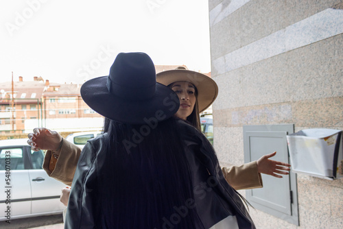 Two friends in hats meeting and giving each other a hug. Two happy female friends hugging and welcoming each other