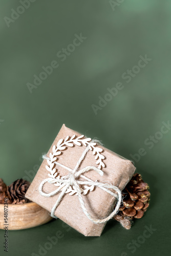 Fototapeta Naklejka Na Ścianę i Meble -  Christmas and zero waste, eco friendly packaging. wrapped gifts in craft paper with pine cones and nut on a green background. ecological Christmas holiday concept, eco decor