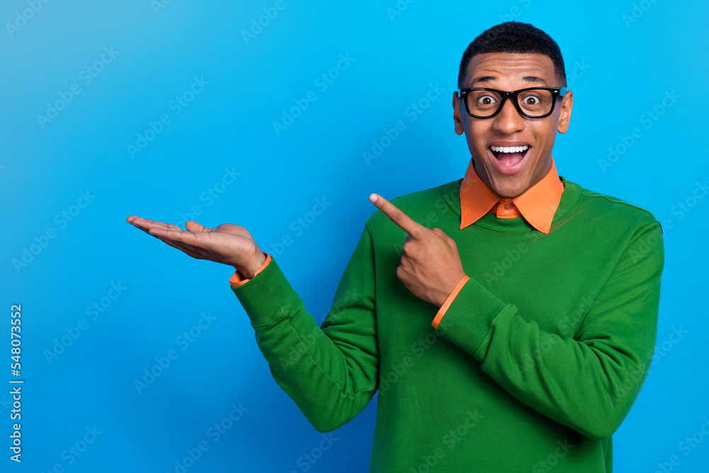 Portrait of ecstatic impressed guy orange shirt under green pullover demonstrate directing empty space isolated on blue color background Portrait of ecstatic impressed guy orange shirt under green pullover demonstrate directing empty space isolated on blue color background