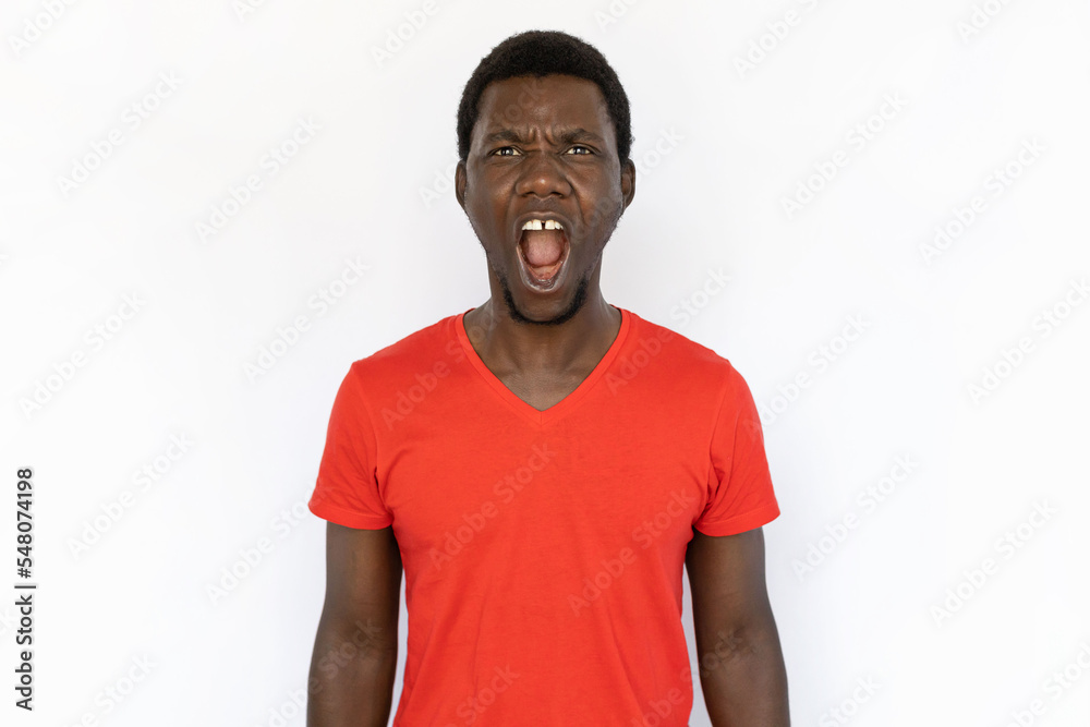 Portrait of angry African American man screaming. Furious young male model with short dark hair in red T-shirt looking at camera, frowning and shouting loudly. Anger, conflict concept Portrait of angry African American man screaming. Furious young male model with short dark hair in red T-shirt looking at camera, frowning and shouting loudly. Anger, conflict concept