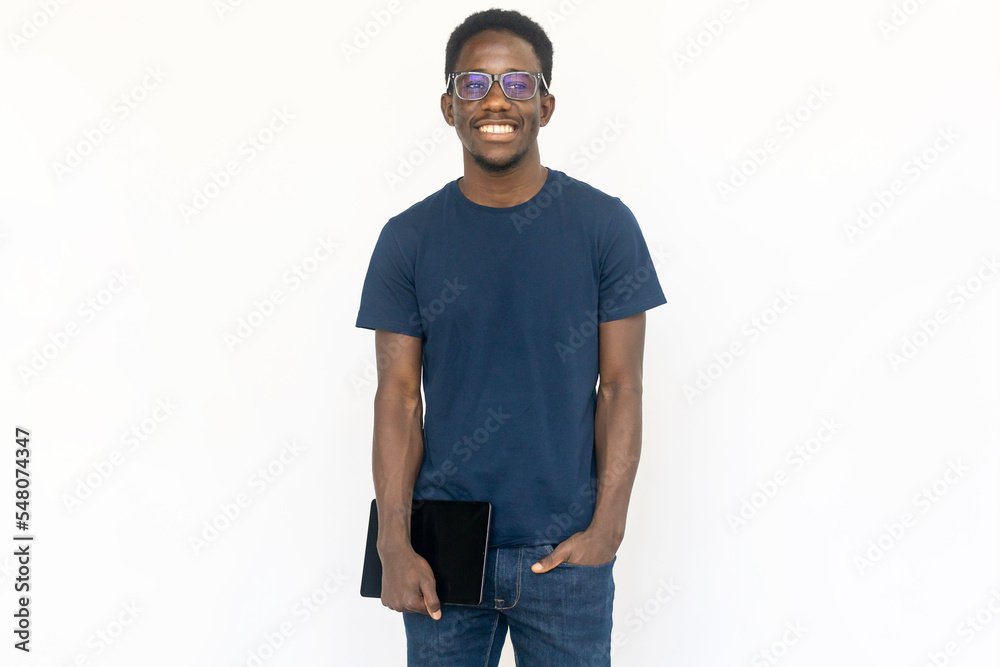 Fototapeta premium Smiling man standing with tablet. Young African American male model holding tablet and smiling with in hand in pocket. Portrait, studio shot, technology concept