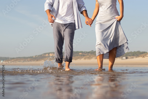 Cropped image of Caucasian couple spending time at beach. Husband and wife in casual clothes running in waves. Vacation, happiness, relationship concept