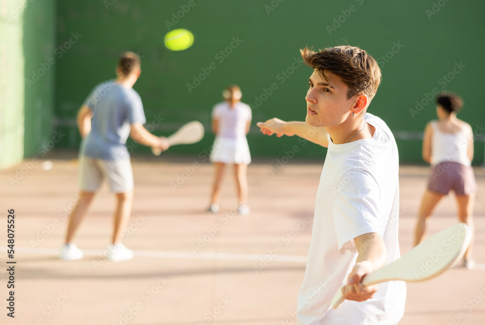 Caucasian young man serving ball with paleta during Basque pelota game outdoors. Boy playing pelota on outdoor fronton.