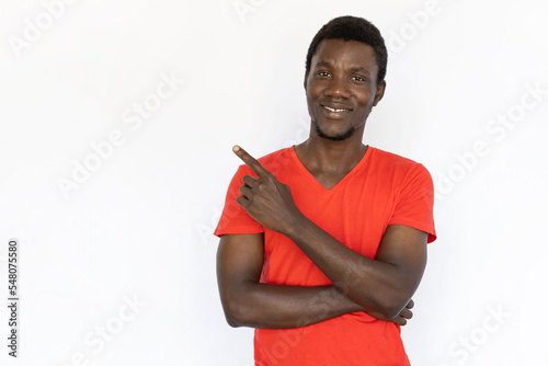 Portrait of cheerful African American man pointing at ad. Happy young male model with short dark hair in red T-shirt looking at camera, showing something with smile. Advertisement concept