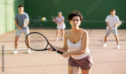 Hispanic woman pelota player hitting ball with racket during training game on outdoor Basque pelota fronton. © JackF