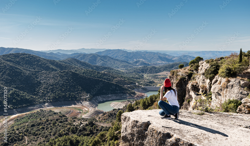 Woman in squatting position on a high mountain reflecting while observing the landscape on the horizon
