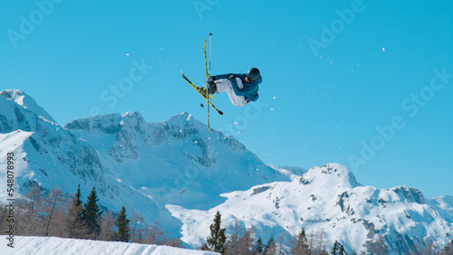 LOW ANGLE VIEW: Male freestyle skier flying above snow-covered mountaintops © helivideo