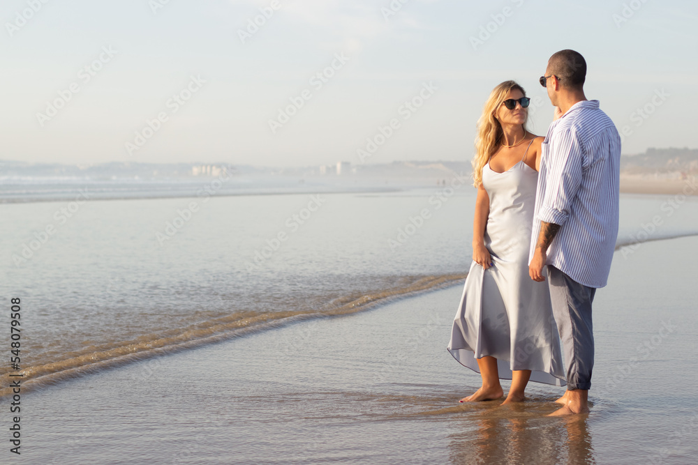 Glad Caucasian couple spending time at beach. Husband and wife in casual clothes walking on wet sand. Travelling, relaxation, happiness, family concept Glad Caucasian couple spending time at beach. Husband and wife in casual clothes walking on wet sand. Travelling, relaxation, happiness, family concept