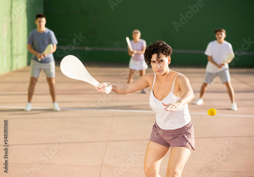 Hispanic woman pelota player hitting ball with wooden racket during training game on outdoor Basque pelota fronton. photo