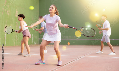 Active fit young hispanic woman playing frontenis on open court on summer day, hitting ball with strung tennis racquet to score to opposing team. Popular Spanish sports..