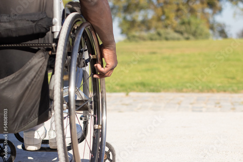 Closeup of muscular male hand touching wheelchair wheel with habitual gesture. Middle-aged man with physical disability spending time outdoors alone. Disability, healthcare, lifestyle concept.