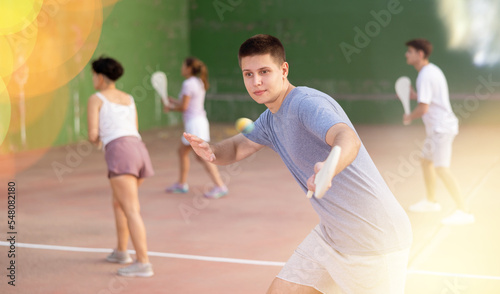Portrait of emotional determined young guy playing pelota at open-air fronton in summer, swinging traditional wooden bat to return ball. Sportsman ready to hit volley © JackF
