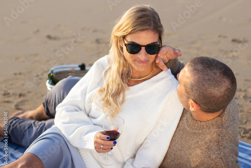 Portrait of tender couple at picnic at sunset. Man and woman in casual clothes sitting and lying on sand, looking at each other. Picnic, meal, love concept © KAMPUS
