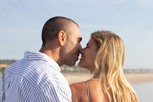 Caucasian couple on summer vacation. Man with shaved head and woman in casual clothes looking at each other, touching with noses tenderly. Love, vacation, affection concept