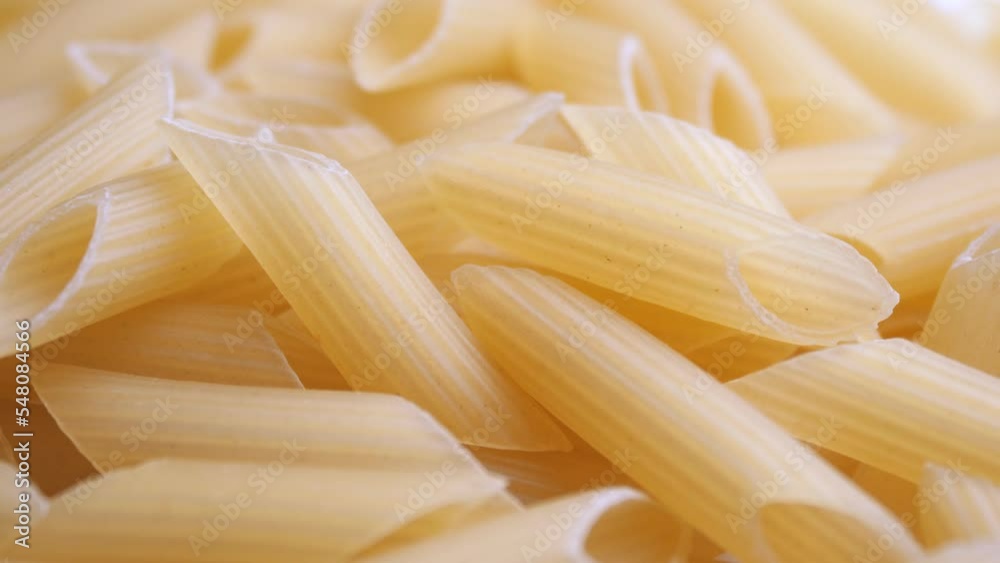 A pile of raw yellow pipe-shaped pasta lies on the surface. Raw pasta feathers in large quantities on the table. A pile of raw yellow pipe-shaped pasta lies on the surface. Raw pasta feathers in large quantities on the table.