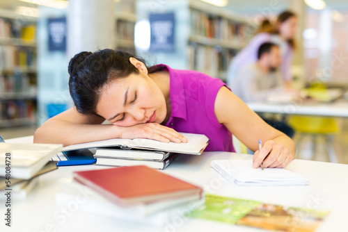 Tired woman resting her head on stack of books in public library