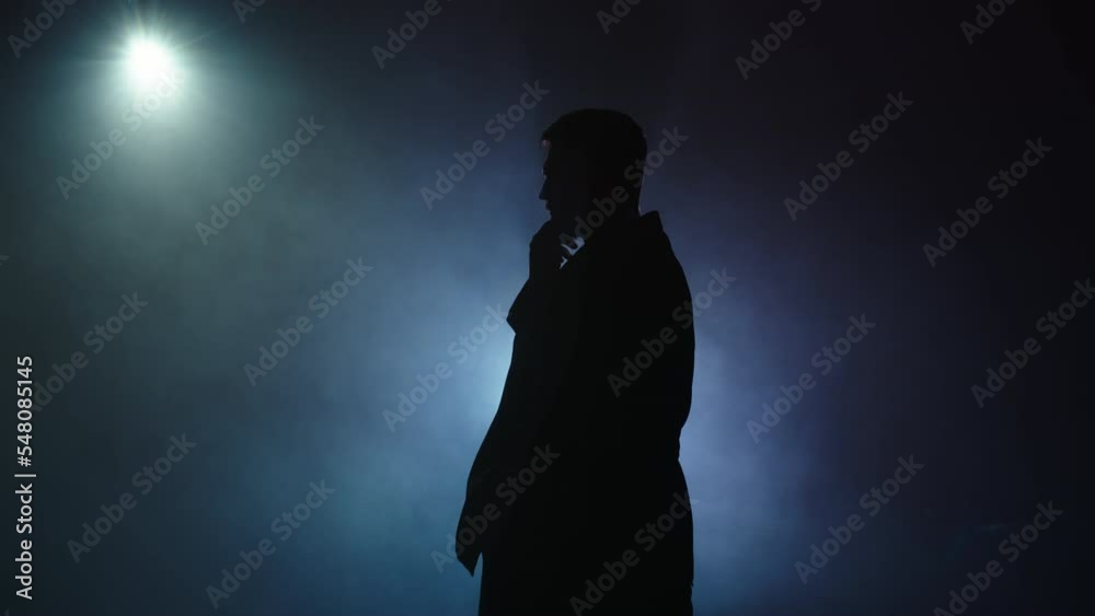 Silhouette of a man in a suit leaves the stage 4K. Mystical atmosphere, smoke, spotlight. Person in the dark Silhouette of a man in a suit leaves the stage 4K. Mystical atmosphere, smoke, spotlight. Person in the dark
