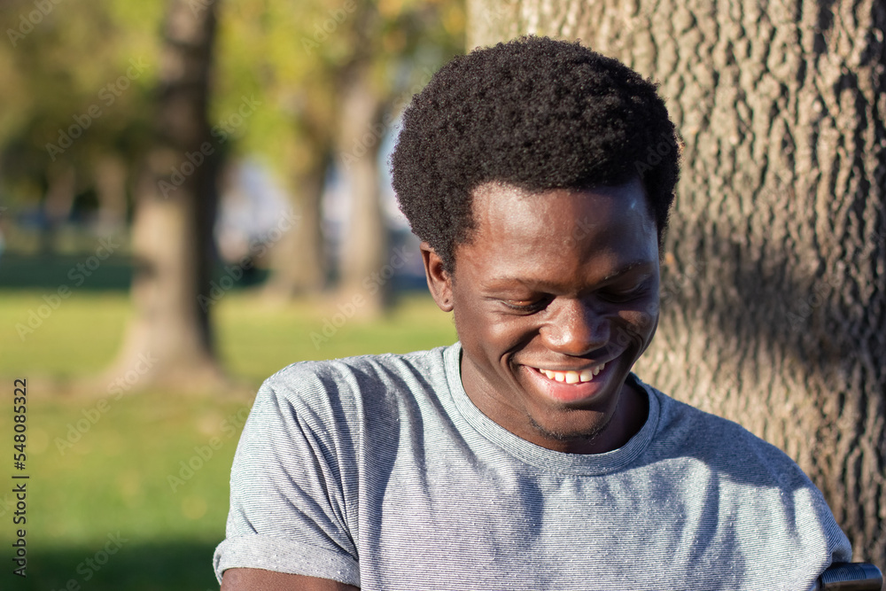 Joyful Black guy spending time outdoors in city park on sunny day. Attractive African American man in grey T-shirt looking down and laughing. Closeup shot. Youth, lifestyle, attitude concept. Joyful Black guy spending time outdoors in city park on sunny day. Attractive African American man in grey T-shirt looking down and laughing. Closeup shot. Youth, lifestyle, attitude concept.