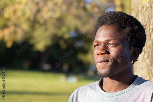 Thoughtful Black guy spending time outdoors in city park. Portrait of handsome African American man in grey T-shirt looking aside and thinking. Closeup shot. Youth, lifestyle, leisure time concept. © KAMPUS