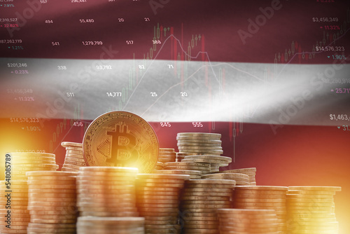 Latvia flag and big amount of golden bitcoin coins and trading platform chart. Crypto currency photo