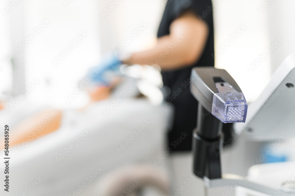 Professional equipment used for facials and other aesthetic procedures. Blurred caucasian dermatologist in black uniform doing facial treatment on her patient. Focus on the foreground. High quality