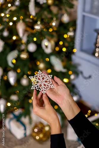 White glitter snowflake in the hands of a girl with blurred and bokeh Christmas tree on background. New Year vibe wallpaper