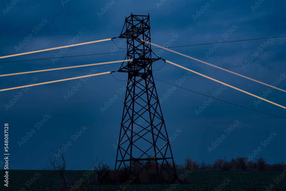 High voltage power transmission tower with luminous wires against a dark night sky