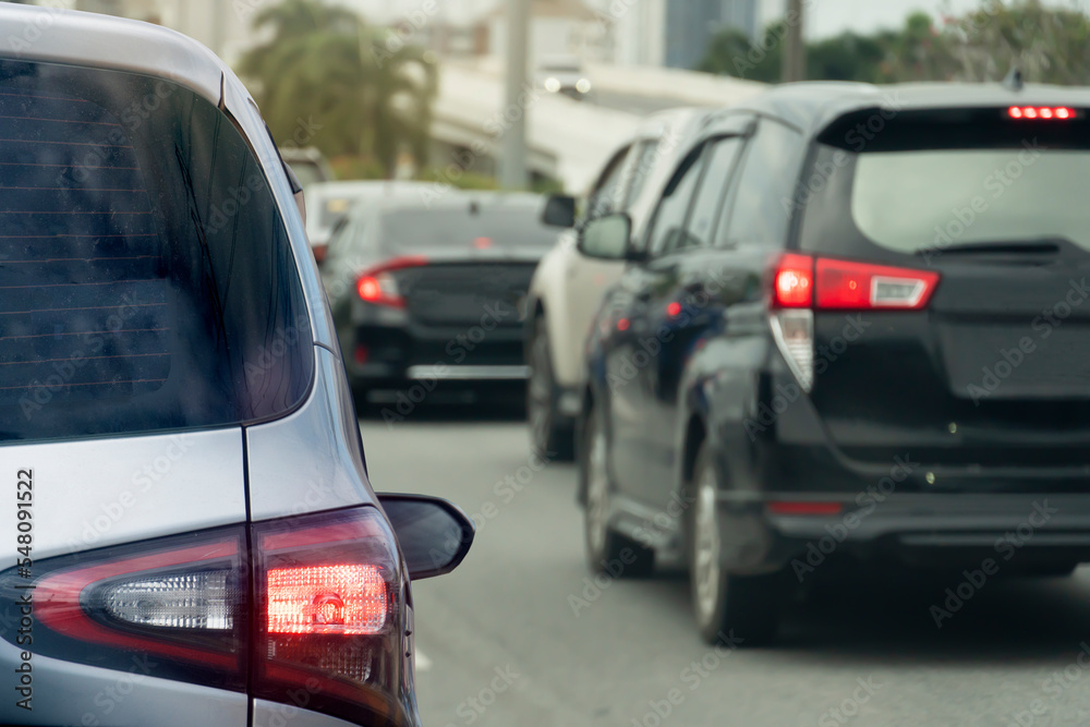 Rear side of silver car on the asphalt road turn on brake light and heading towards the goal of the trip. Traveling for work during rush hour. Environment blurred of other cars during the day.