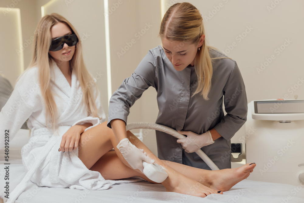 Beautician removes hair on beautiful female legs using a laser hair removal in Beauty clinic Beautician removes hair on beautiful female legs using a laser hair removal in Beauty clinic
