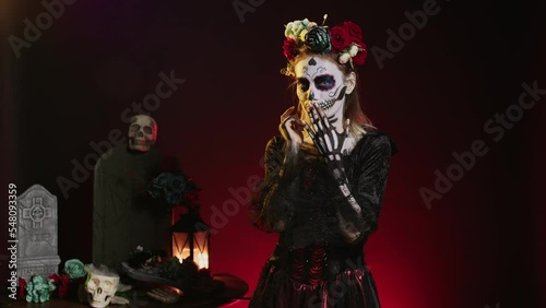 Young scary woman doing hush gesture to keep secret, wearing santa muerte costume and showing slience mute and secrecy sign with finger over lips. Holy dios de los muertos holiday. photo