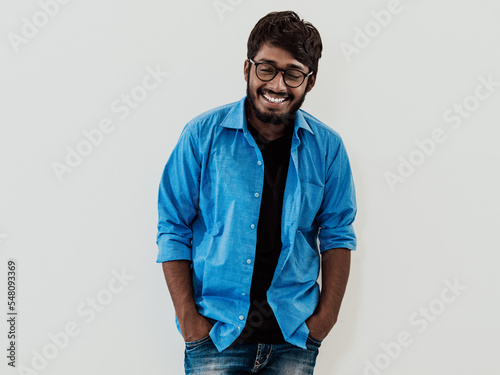 Indian smiling young man with blue shirt and glasses posing on gray background