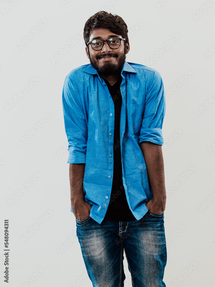Fototapeta premium Indian smiling young man with blue shirt and glasses posing on gray background