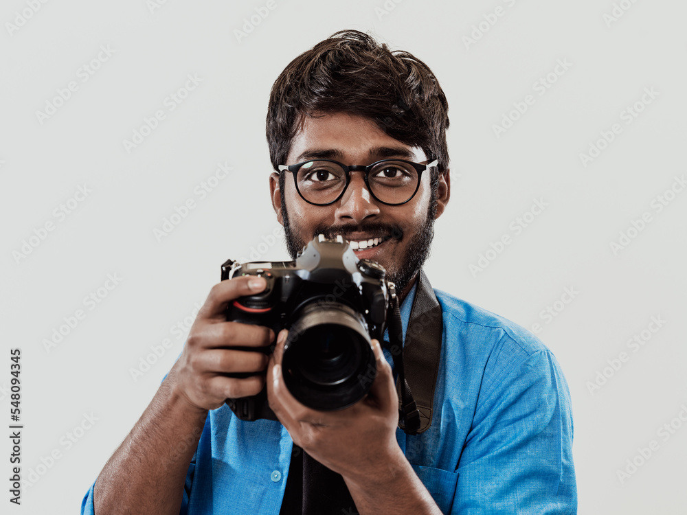 Professional photographer having DSLR camera taking picture.Indian man photography enthusiast taking photo while standing on blue background. Studio shot Professional photographer having DSLR camera taking picture.Indian man photography enthusiast taking photo while standing on blue background. Studio shot