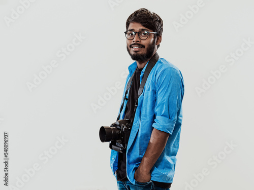 Professional photographer having DSLR camera taking picture.Indian man photography enthusiast taking photo while standing on blue background. Studio shot