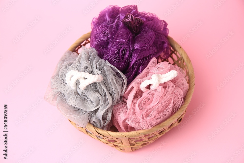 Wicker basket with colorful shower puffs on pink background, above view Wicker basket with colorful shower puffs on pink background, above view