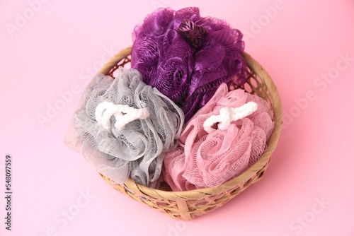 Wicker basket with colorful shower puffs on pink background, above view