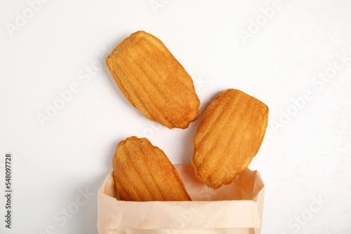 Paper bag with delicious madeleine cakes on white background, flat lay photo