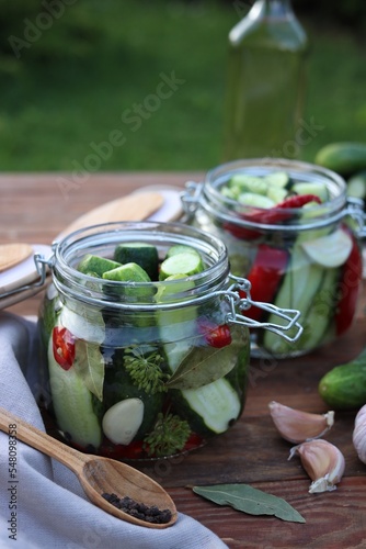 Glass jars with fresh cucumbers and other ingredients on wooden table. Canning vegetables