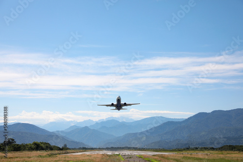 Modern white airplane landing on runway near mountains