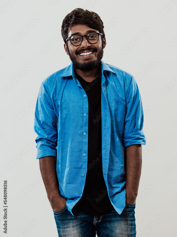 Fototapeta premium Indian smiling young man with blue shirt and glasses posing on gray background