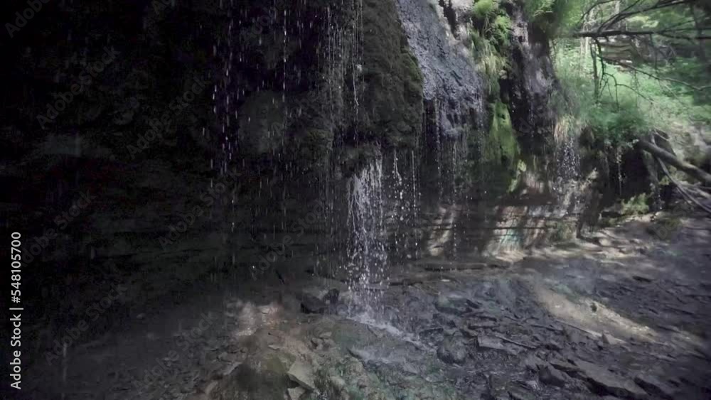 Slow motion view of a waterfall with crystal clear water running down a rocky wall and a cave at the base Slow motion view of a waterfall with crystal clear water running down a rocky wall and a cave at the base