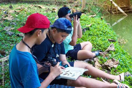 Asian boy and friends Invite each other to see birds in the community forest on holidays. And help each other to search for the types of birds found from the birds Guide book. photo