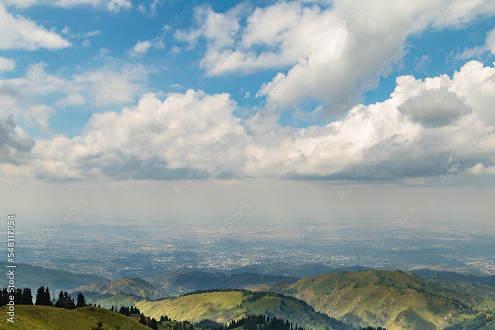 View from the mountains to the city of Almaty in the distance under a blue sky with clouds. Ecology of the city, copy space.