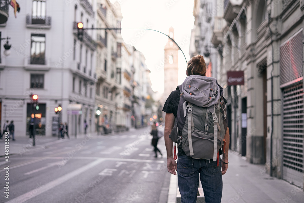 young caucasian man standing with his back on a city street with a large backpack on his back, valencia, spain