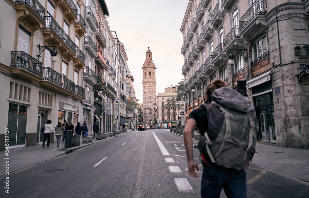 young caucasian man with big backpack on his back walking on a city street, valencia, spain