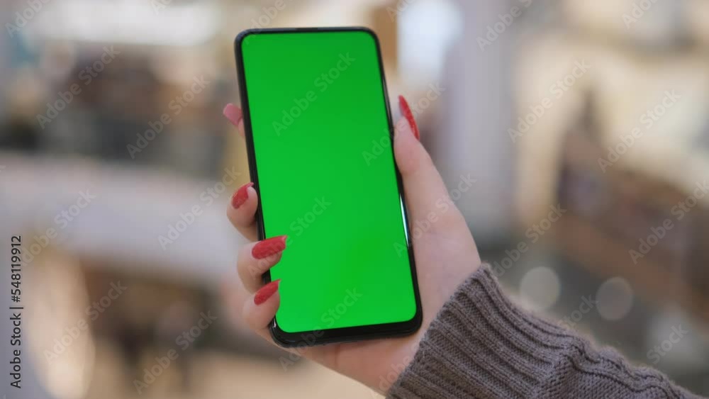 Mall. Shopping center. Department store. Back view of brunette holding chroma key green screen smartphone watching content. Shopping online. Gadgets and contemporary people concept. 4K Mall. Shopping center. Department store. Back view of brunette holding chroma key green screen smartphone watching content. Shopping online. Gadgets and contemporary people concept. 4K