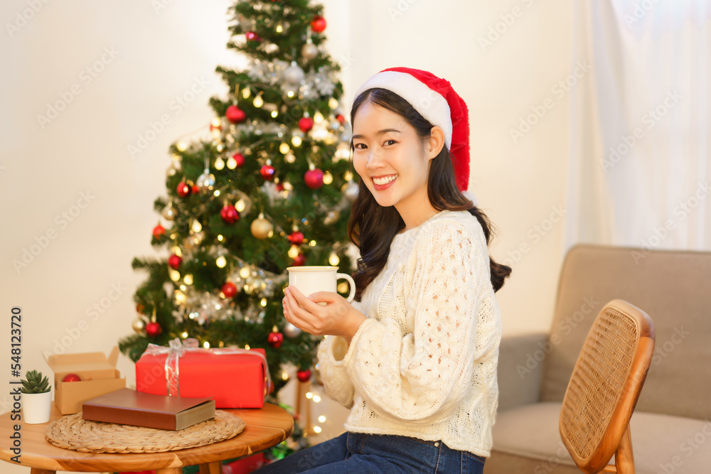 Christmas concept, Young asian woman sitting on chair near christmas tree and holding coffee cup Christmas concept, Young asian woman sitting on chair near christmas tree and holding coffee cup
