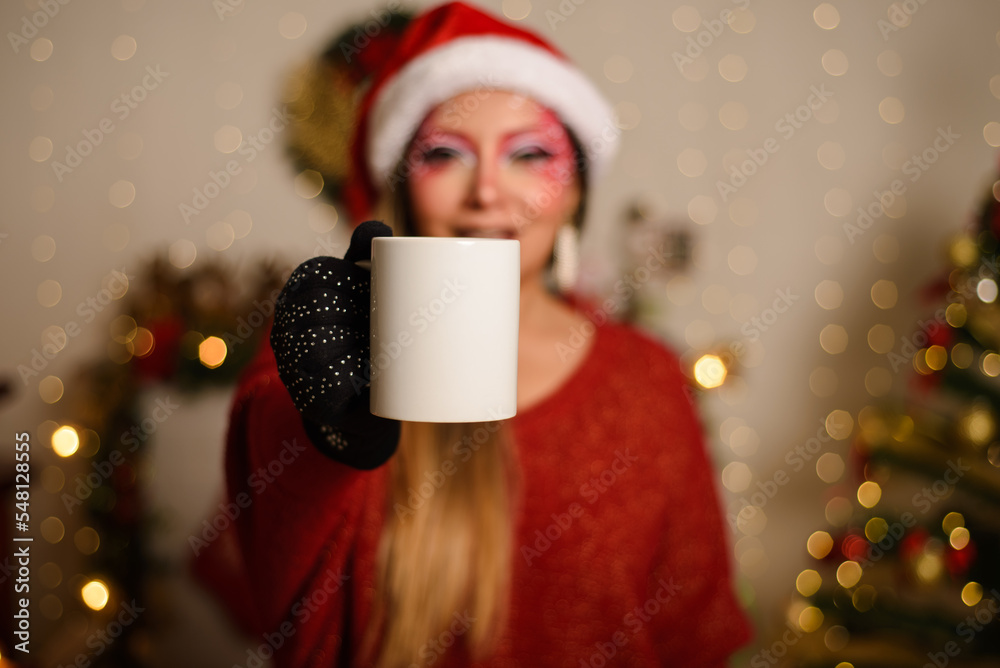 Young woman with Christmas fantasy makeup holding white mug. Selective focus on the mug. Christmas background. Young woman with Christmas fantasy makeup holding white mug. Selective focus on the mug. Christmas background.