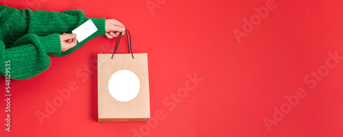 Xmas shopping concept. Woman's hands holding a gift bag and a credit card on a red background,