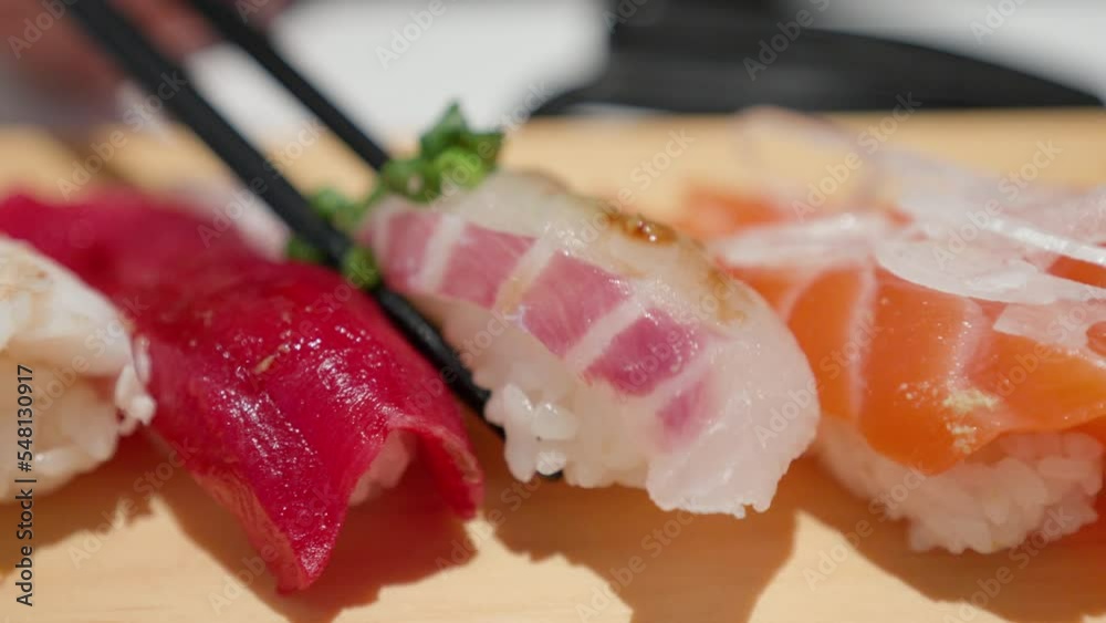 Chopsticks picks up piece of whitefish sushi, or Shiromi from sushi board. Chopsticks picks up piece of whitefish sushi, or Shiromi from sushi board.